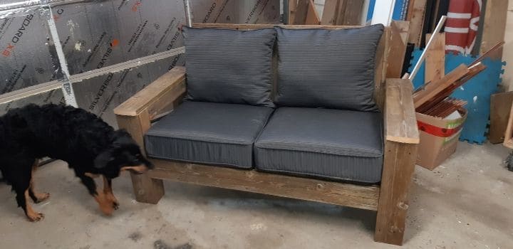 Assembled reclaimed wood outdoor love seat with grey cushions and dog ready to jump on
